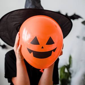 Image of a child holding a bright orange Halloween pumpkin face balloon.
